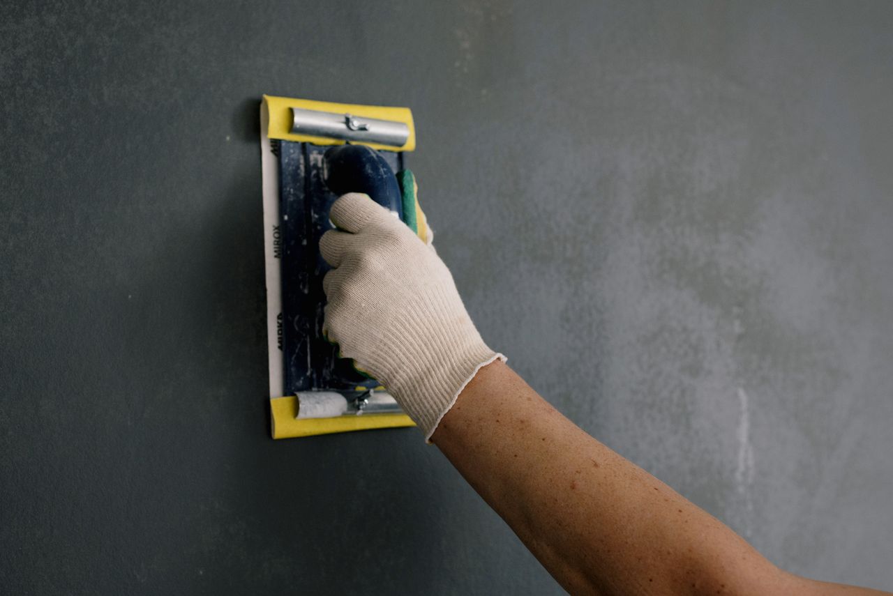 Crop unrecognizable male in white gloves holding scraper and renovating walls in apartment